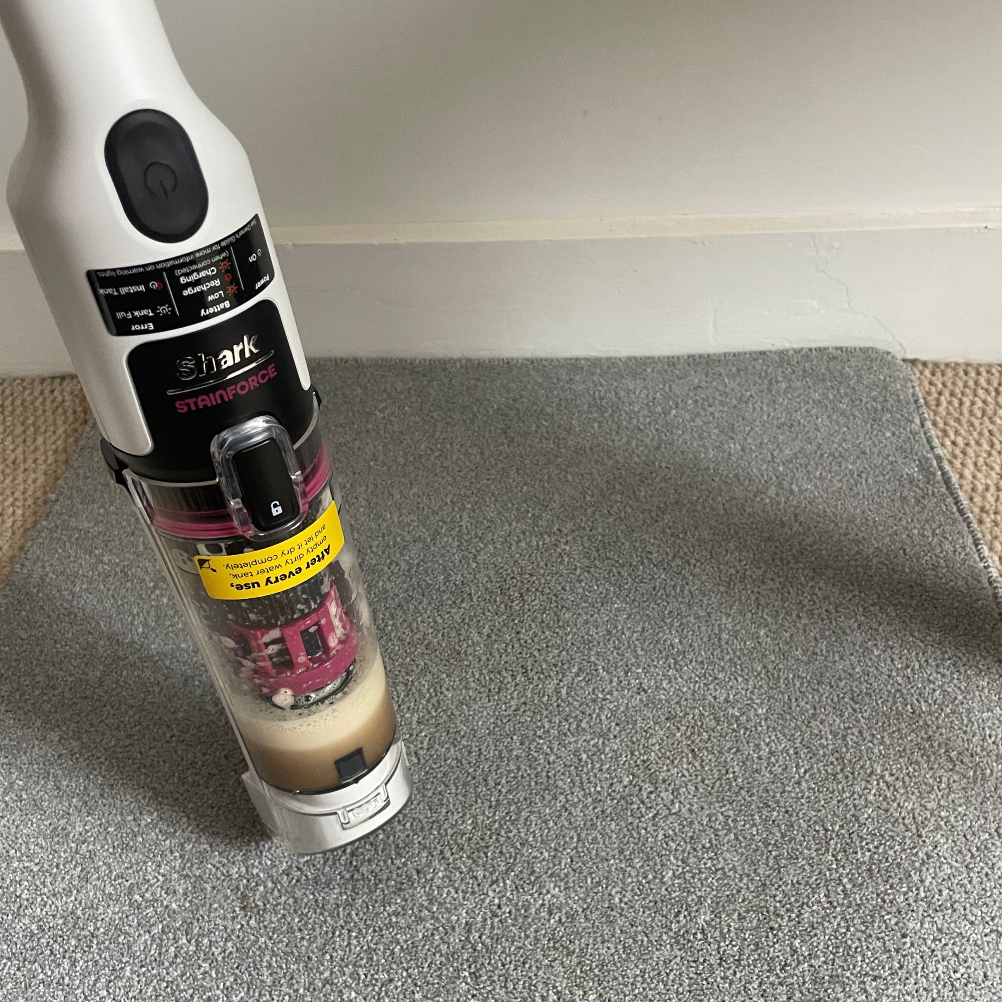 Shark Stainforce Spot Cleaner with dirty water in the chamber, standing on a grey carpet sample