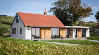 modern home with white rendered walls, tiled roof, aluminium framed windows and doors and garage next to it converted and finished in same materials