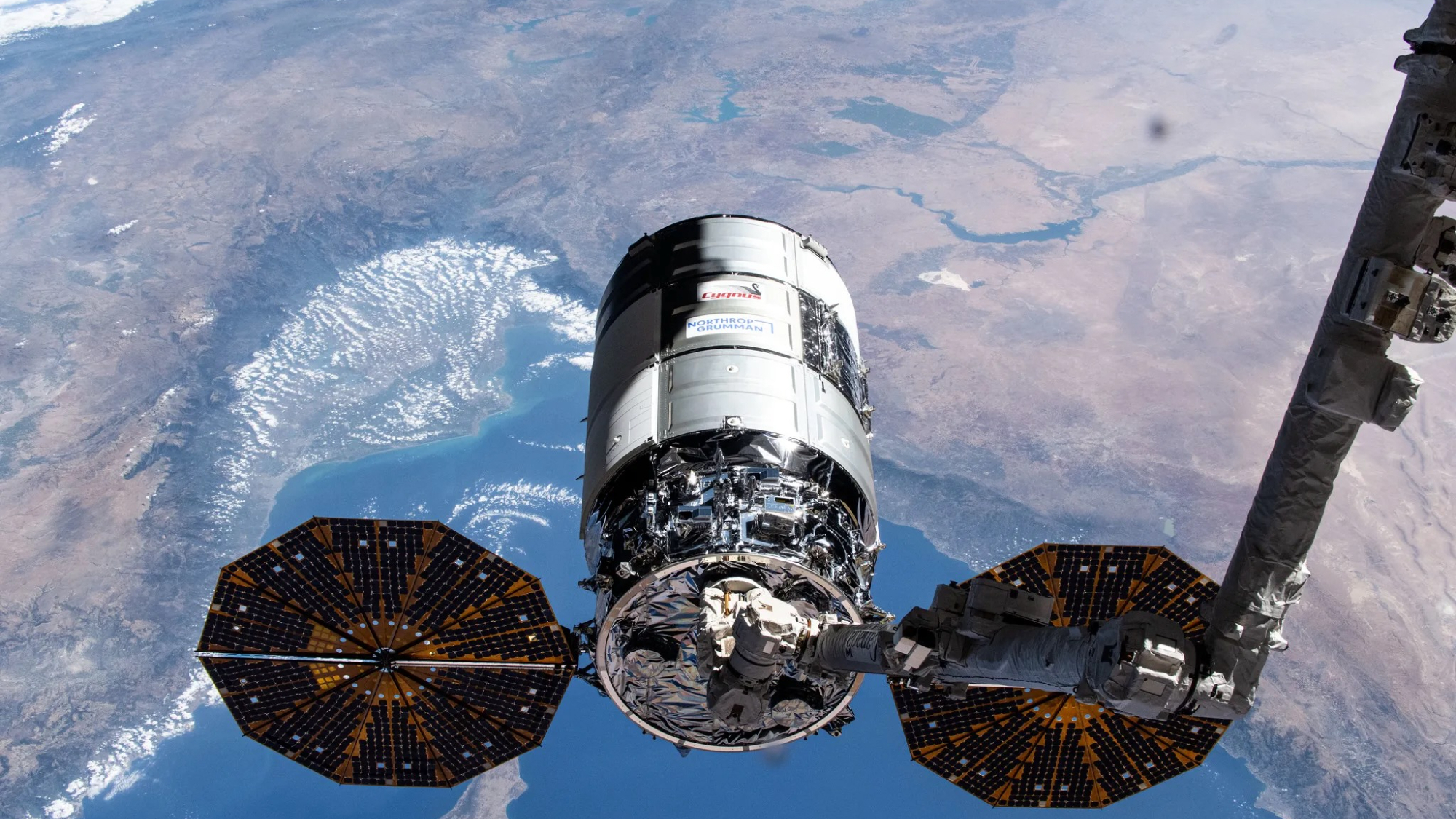 Northrop Grumman’s 21st Cygnus cargo craft, with its prominent cymbal-shaped UltraFlex solar arrays, is pictured in the grips of the Canadarm2 robotic arm shortly after its capture on Aug. 6, 2024.