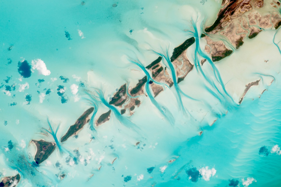 Fluffy white clouds and turquoise crystal waters are visible from space in this astronaut photograph of the Bahamas taken on July 15, 2015. The picture is so detailed that a jet can be seen flying across the large channel in the upper right quadrant of the photo.