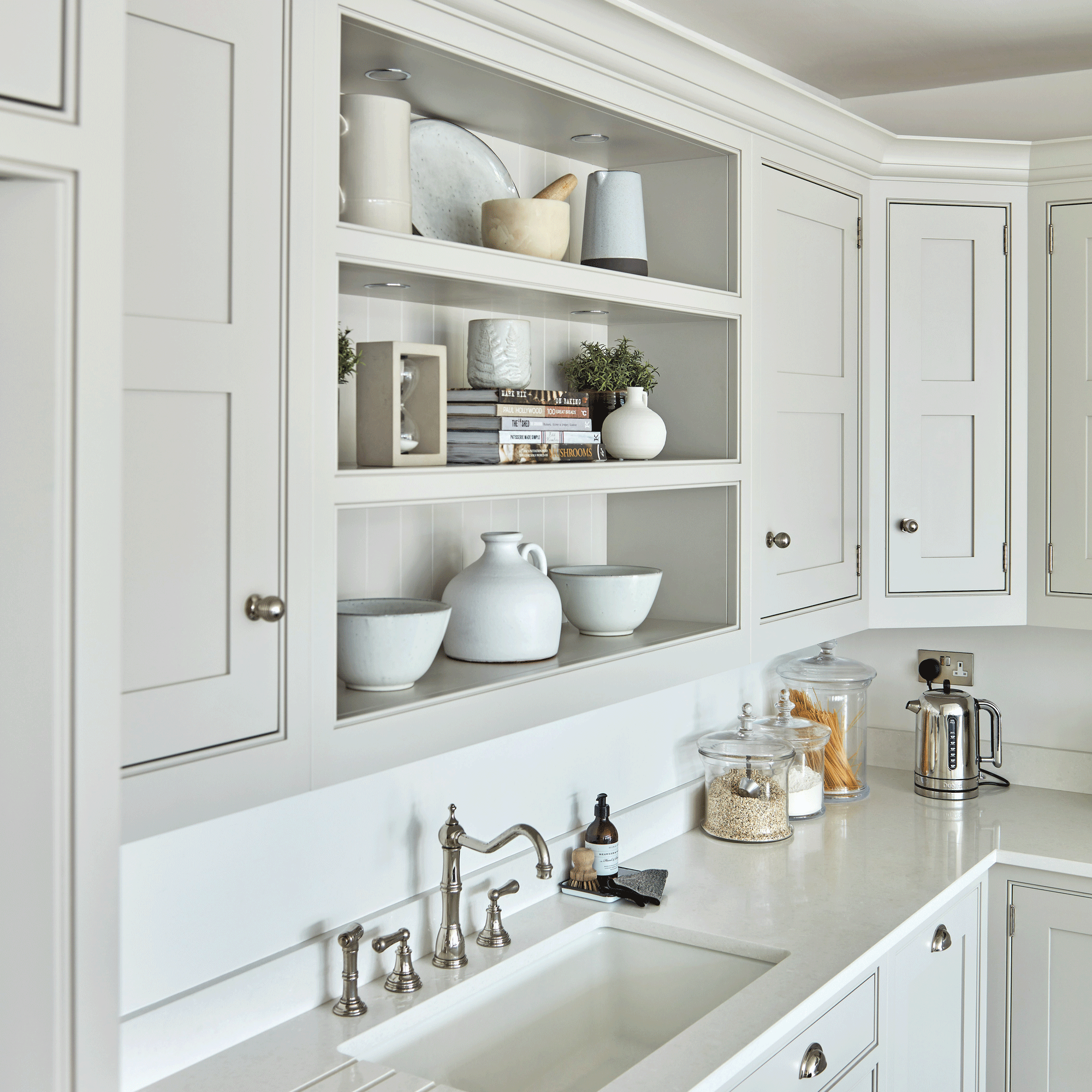 White kitchen cabinets with white open shelving in the middle over a sink.