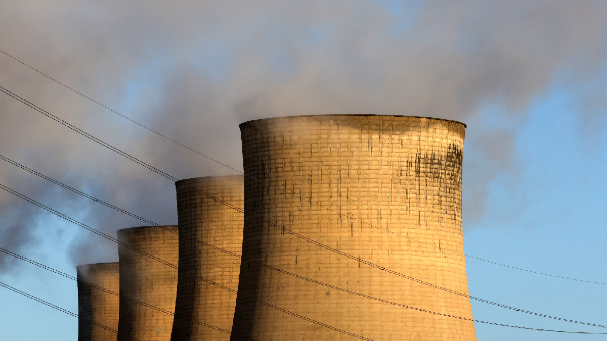 A line of four nuclear power plant cooling towers are foregrounded by numerous powerlines.