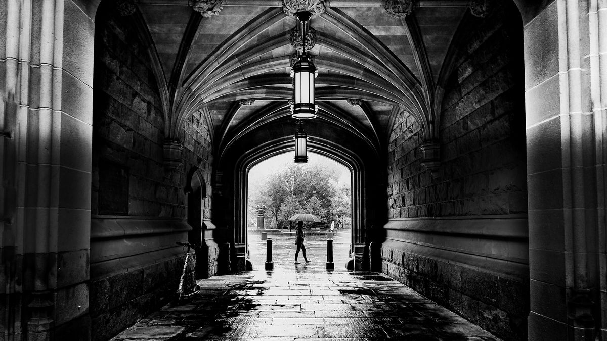 Black and white image of a person walking under an archway with hanging lanterns