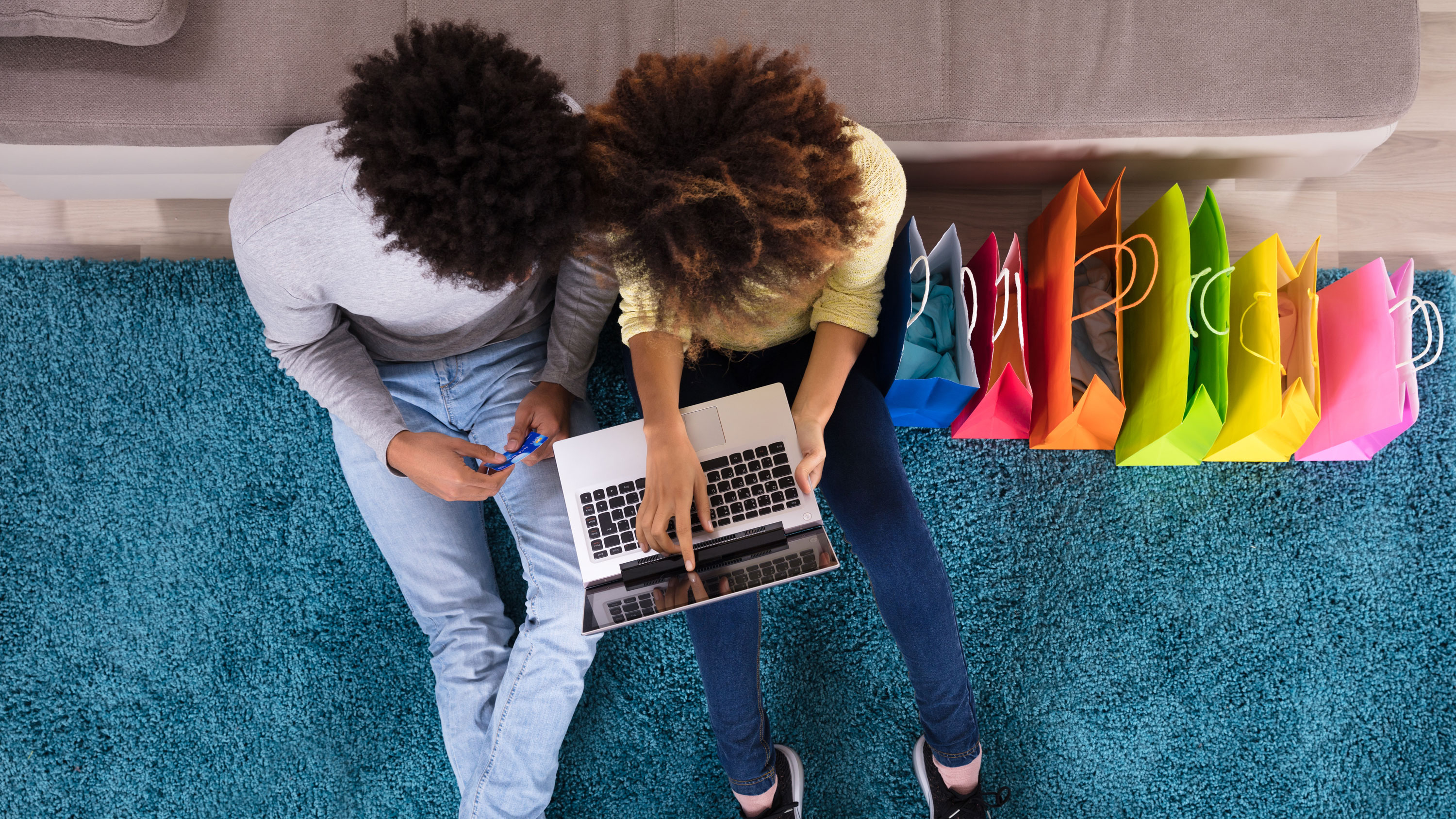 Jeune Couple Shopping En Ligne Sur Ordinateur Portable Avec Des Sacs À Provisions Multicolores Sur Canapé