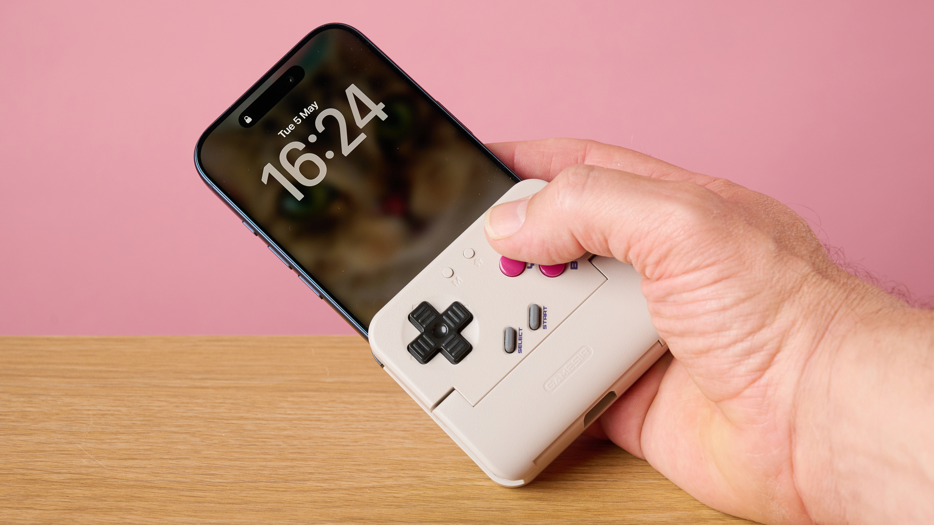 A man's hand holding an iPhone 17 Pro plugged into the GameSir Pocket Taco.