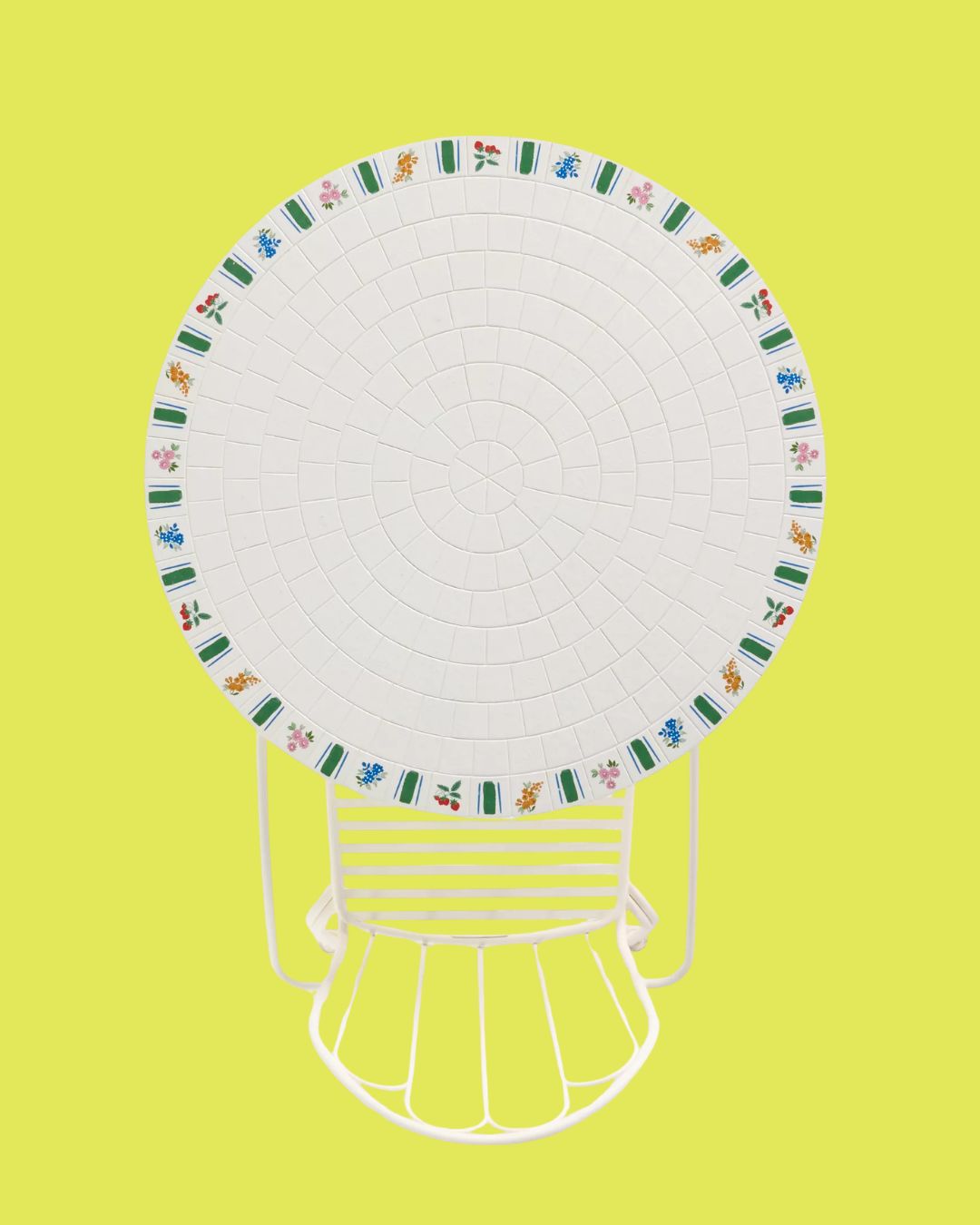 White Bisou Tile Bistro Outdoor Table with floral motifs and round structure, paired with a thin, white-painted iron chair, placed against a yellow background.