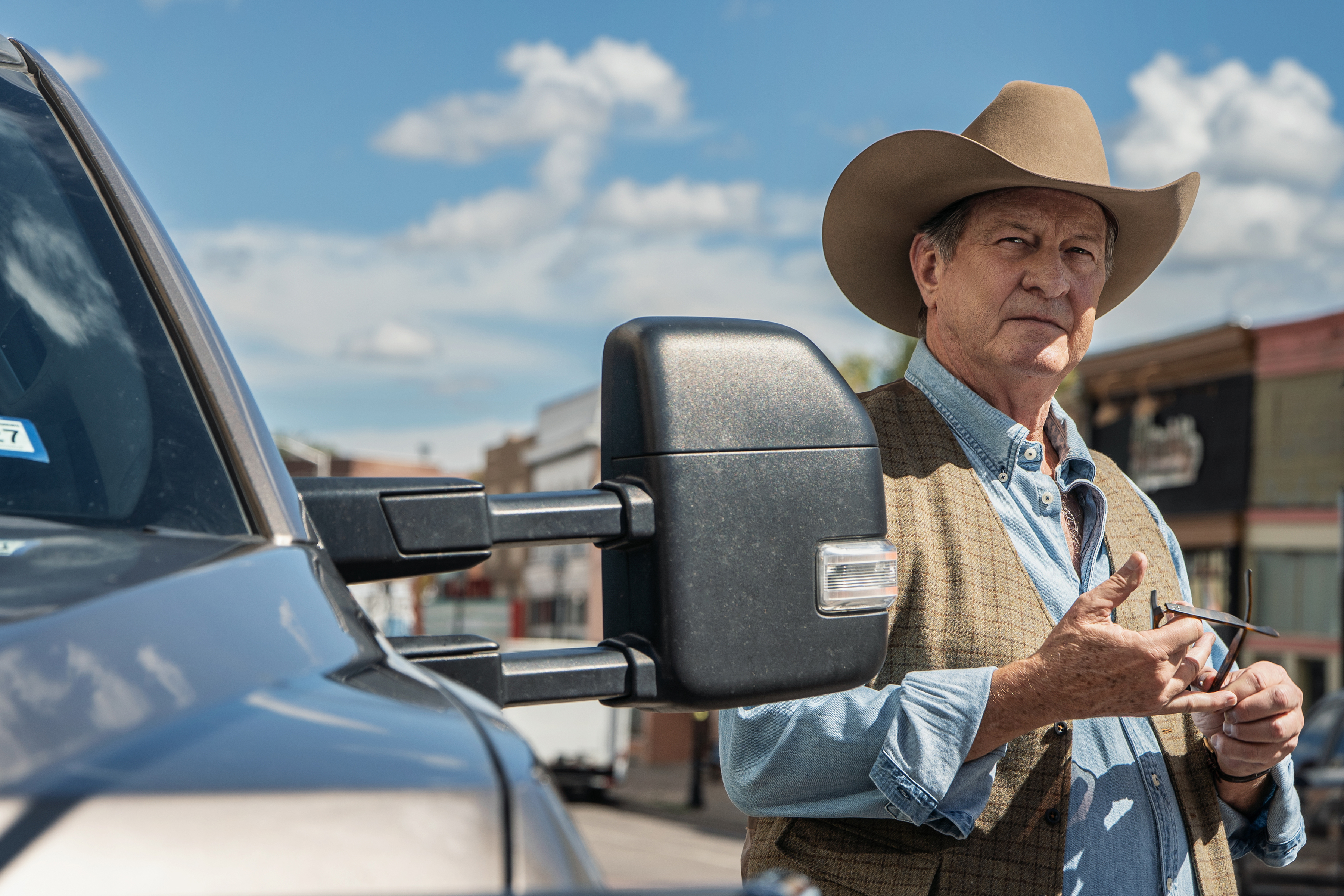 Brett Cullen as Sam Kirkland stands to the right of a pickup truck while holding a piece of metal, in Episode 203 of Netflix's 'Ransom Canyon' Season 2.