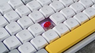 A photo of the NuPhy Air75 V2 with the F keycap removed to show a red switch and RGB lighting,on a stone slab with a blue wall in the background.