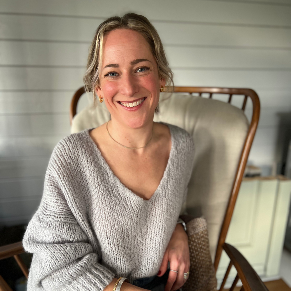 female with blond hair wearing v necked jumper sat on chair