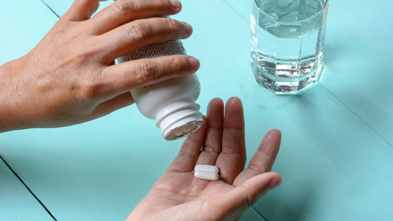 Person taking a supplement with a glass of water