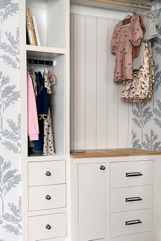 A kids closet with open doors revealing clothes, and a small whole for a laundry chute on the surface
