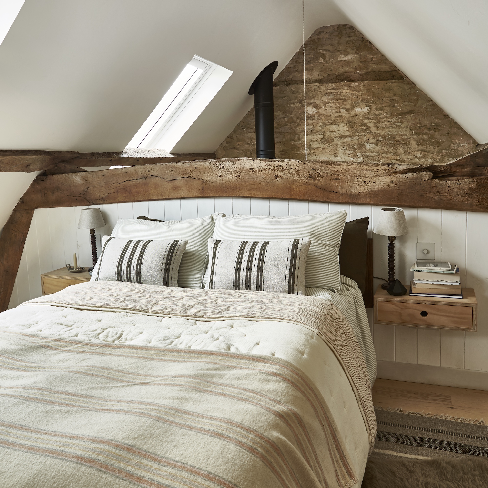 double bed in mezzanine of small cottage, with striped bed linen