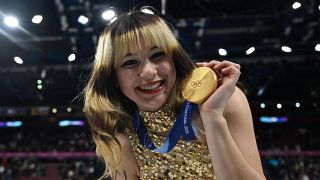 Alysa Liu holds her individual gold medal at Milan Cortina after her figure skating win in her sparkly gold dress.