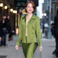Emma Stone wearing a long sleeved green skirt set. She has a short, bob haircut and is smiling at the camera.