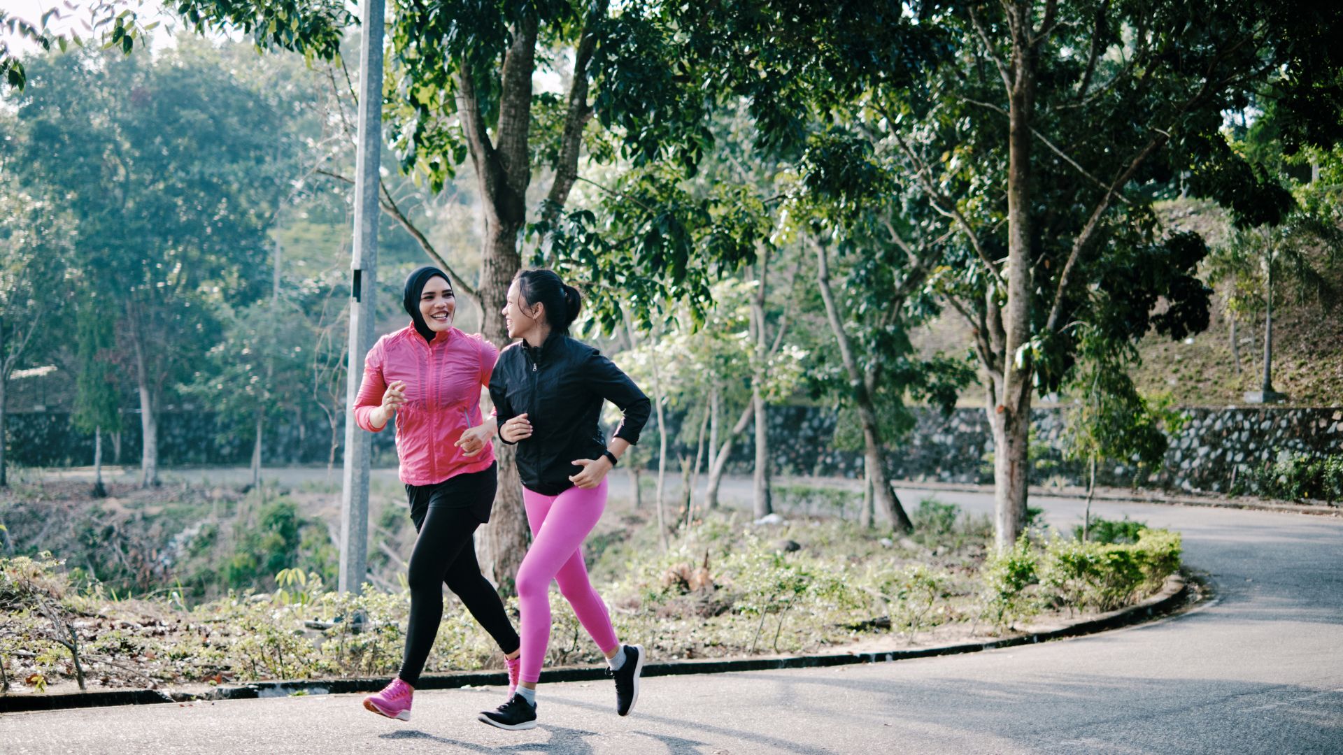 Two women running together in the park along a path laughing and smiling