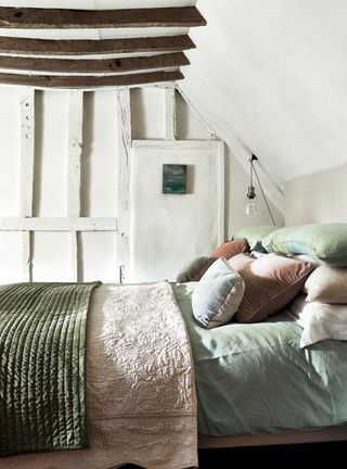 cottage bedroom with painted white timbers and green and pink bed linen and sloping ceiling