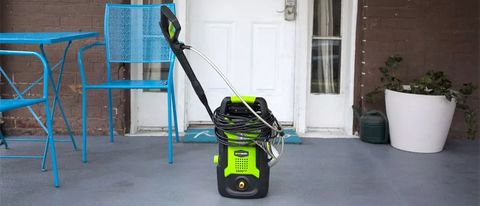 The Greenworks GPW1501 pressure washer unit in front of a white door and blue outdoor chair