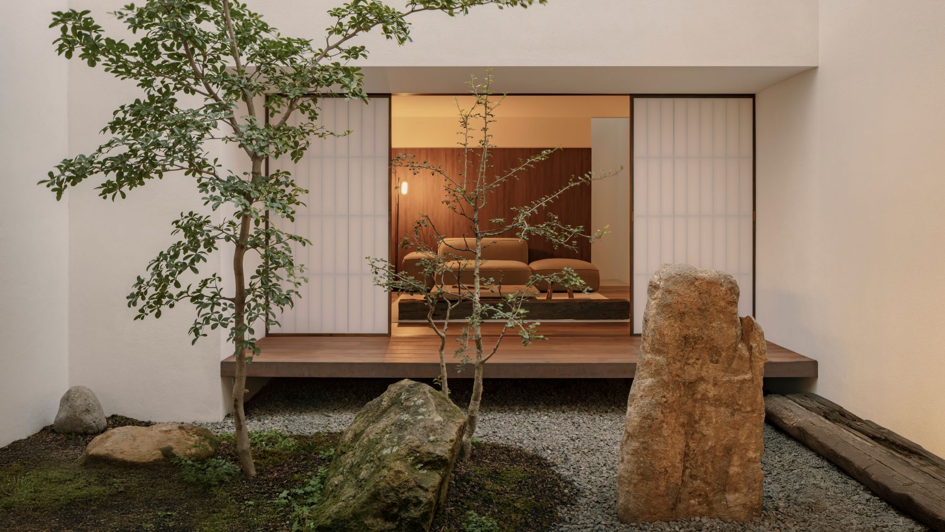 A courtyard garden with two trees, a mossy ground cover and a rock with a vide of a Japanese living room