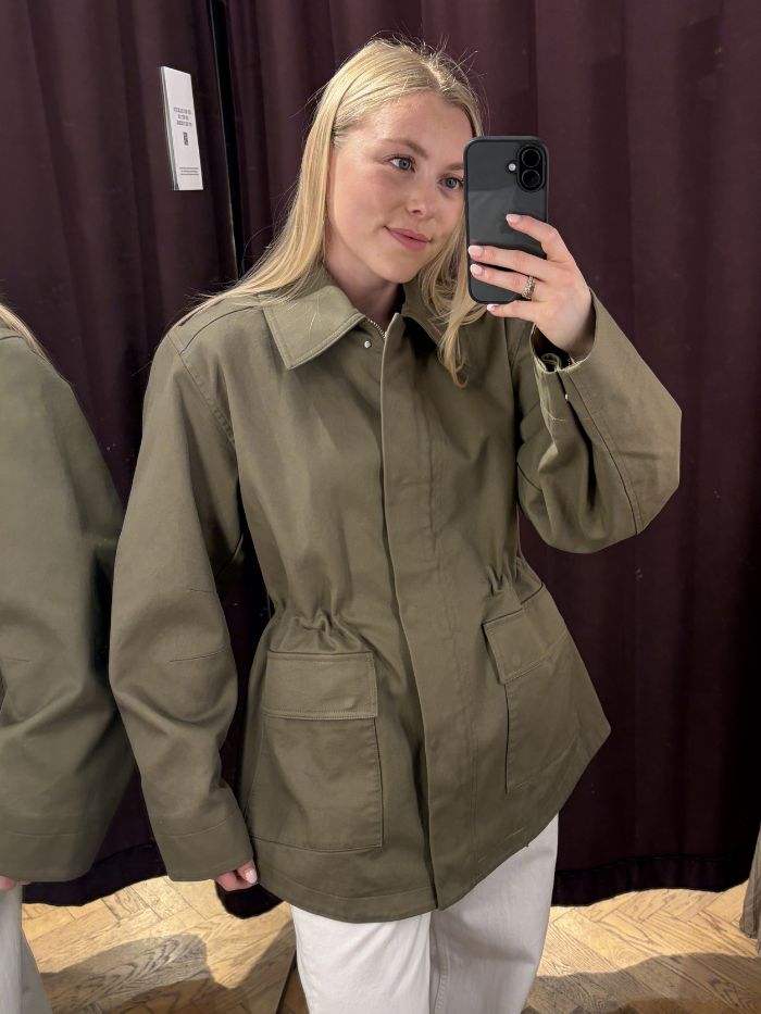 Woman wears green cinched waist jacket and white jeans