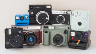 A selection of instant cameras from Polaroid, Instax and Lomography stacked up, in front of a white background