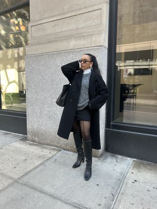 Lauren Tappan wearing a white shirt, gray sweater, black coat, black mini skirt, tights, and boots