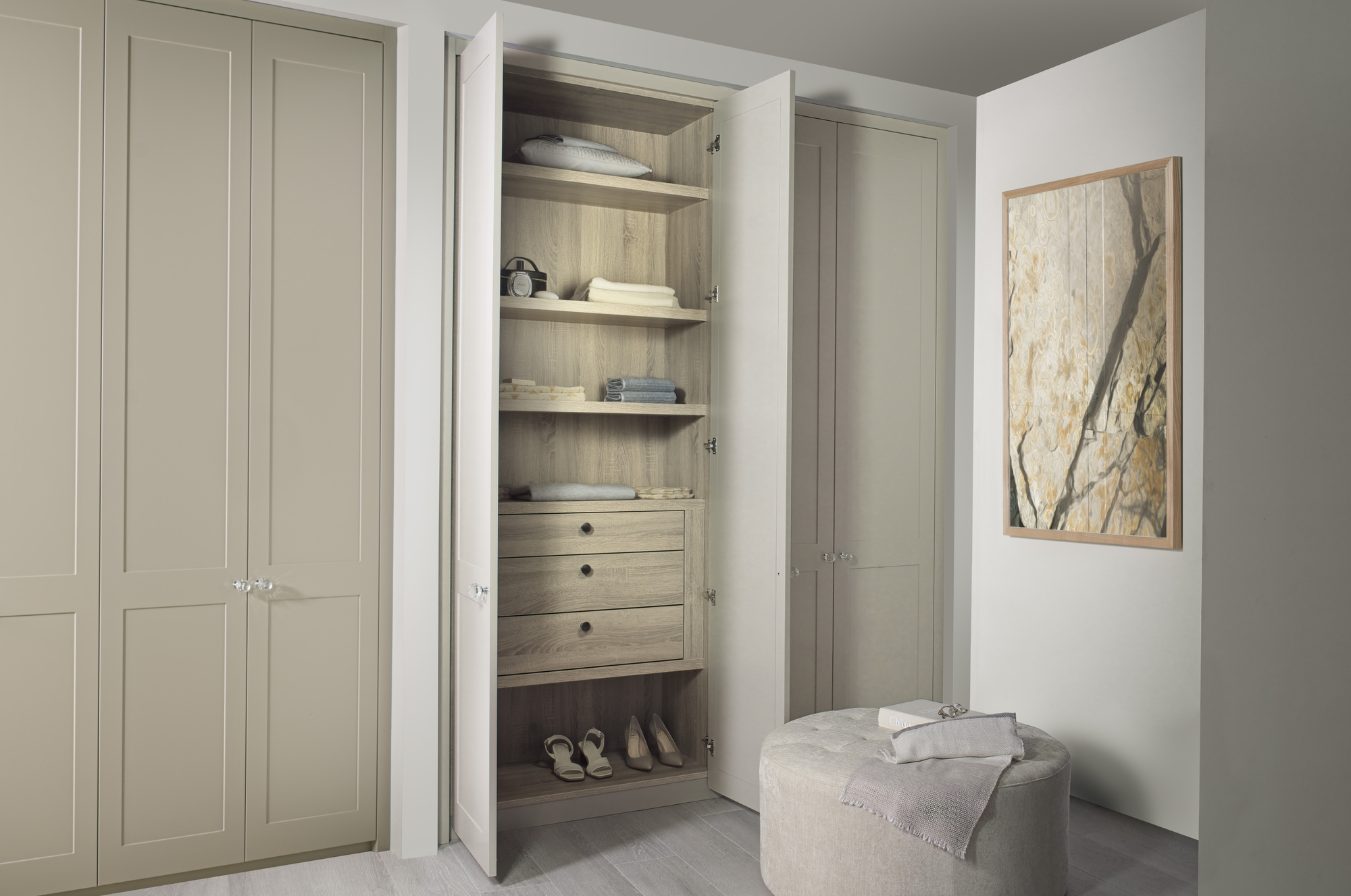 A neutral closet with shaker doors painted greige, organized wood-effect shelves, and a stool