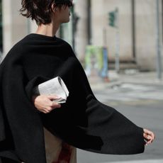 A model wearing a Zara black cape holding a newspaper and wearing a printed skirt.