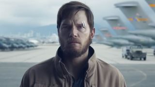 Chris Pratt standing in an airport hanger. 