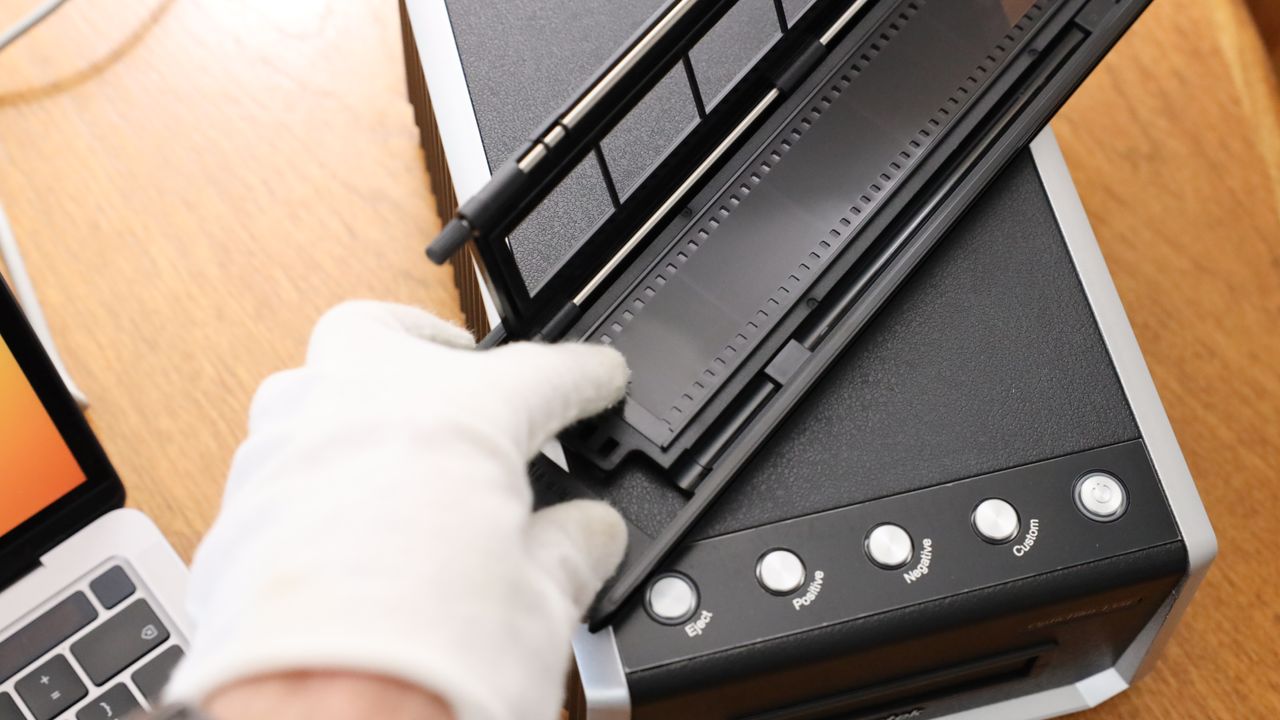 A hand in a white glove putting a strip of film into a film holder for the Plustek OpticFilm 135i