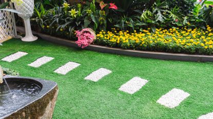 A small garden with artificial grass and borders with colourful flowers