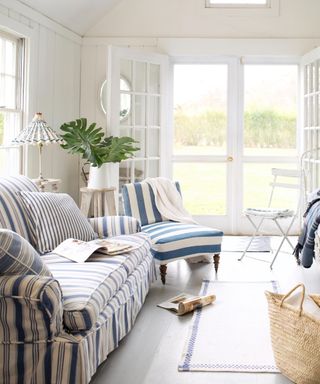 living room with white walls, sloped ceiling, blue and white striped sofa and armchair, glass doors leading to garden