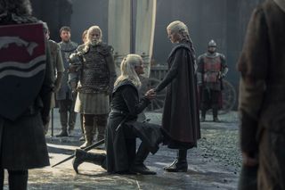 A knight (Matt Smith as Daemon Targaryen, center) kneels to a woman (Emma D'Arcy as Rhaenyra Targaryen) in the middle of a crowded castle chamber, in 'House of the Dragon' season 2.