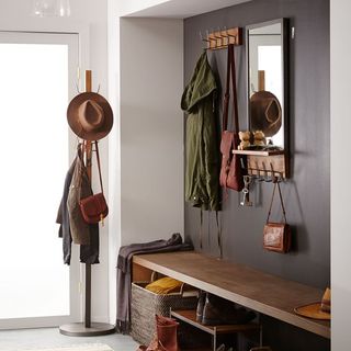a mudroom idea with a long wooden bench, wall hooks for coats and accessories and a mirror on the wall