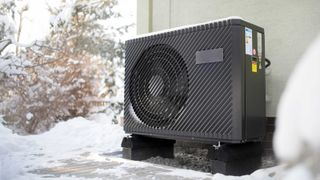 Black air source heat pump outside unit next to house and snow covered path and garden