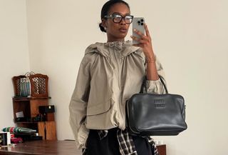 Woman in beige anorak holding a phone and black bag