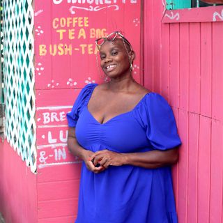 Andi Oliversmiling wearing a blue dress in front of a pink wall