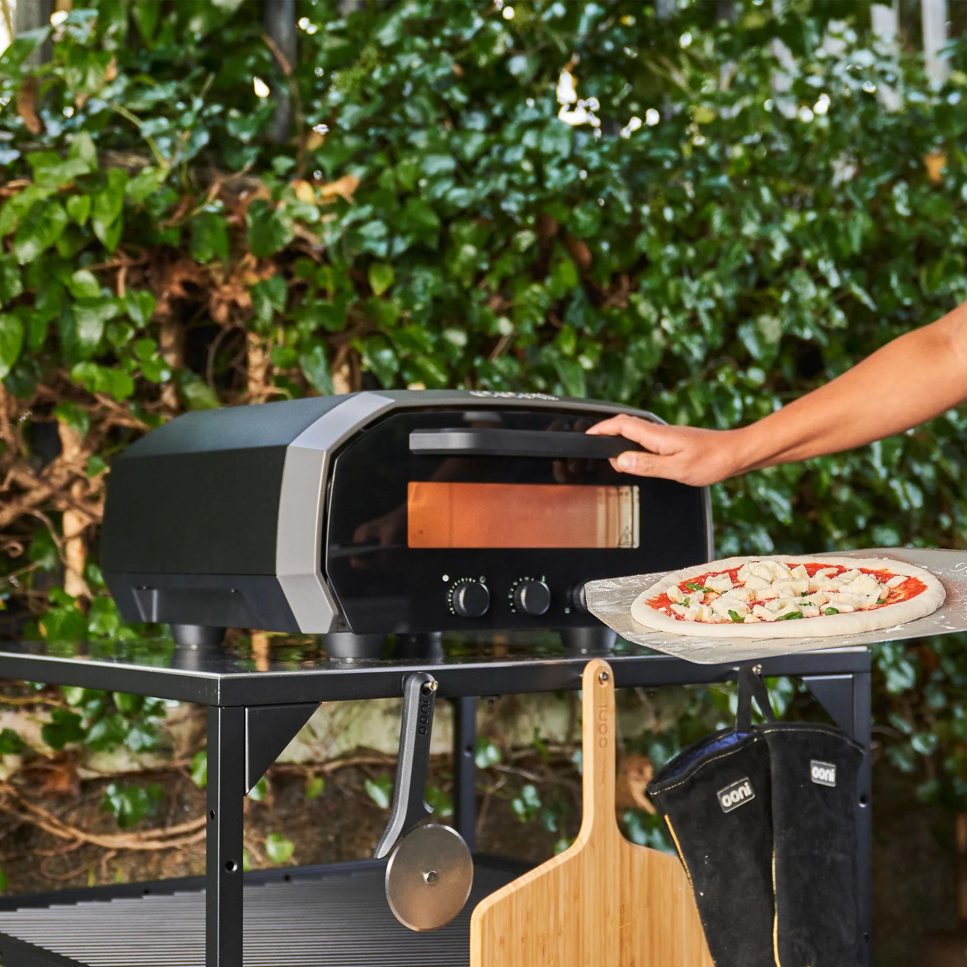 Ooni Volt pizza oven in promo image being used outside on a pizza stand