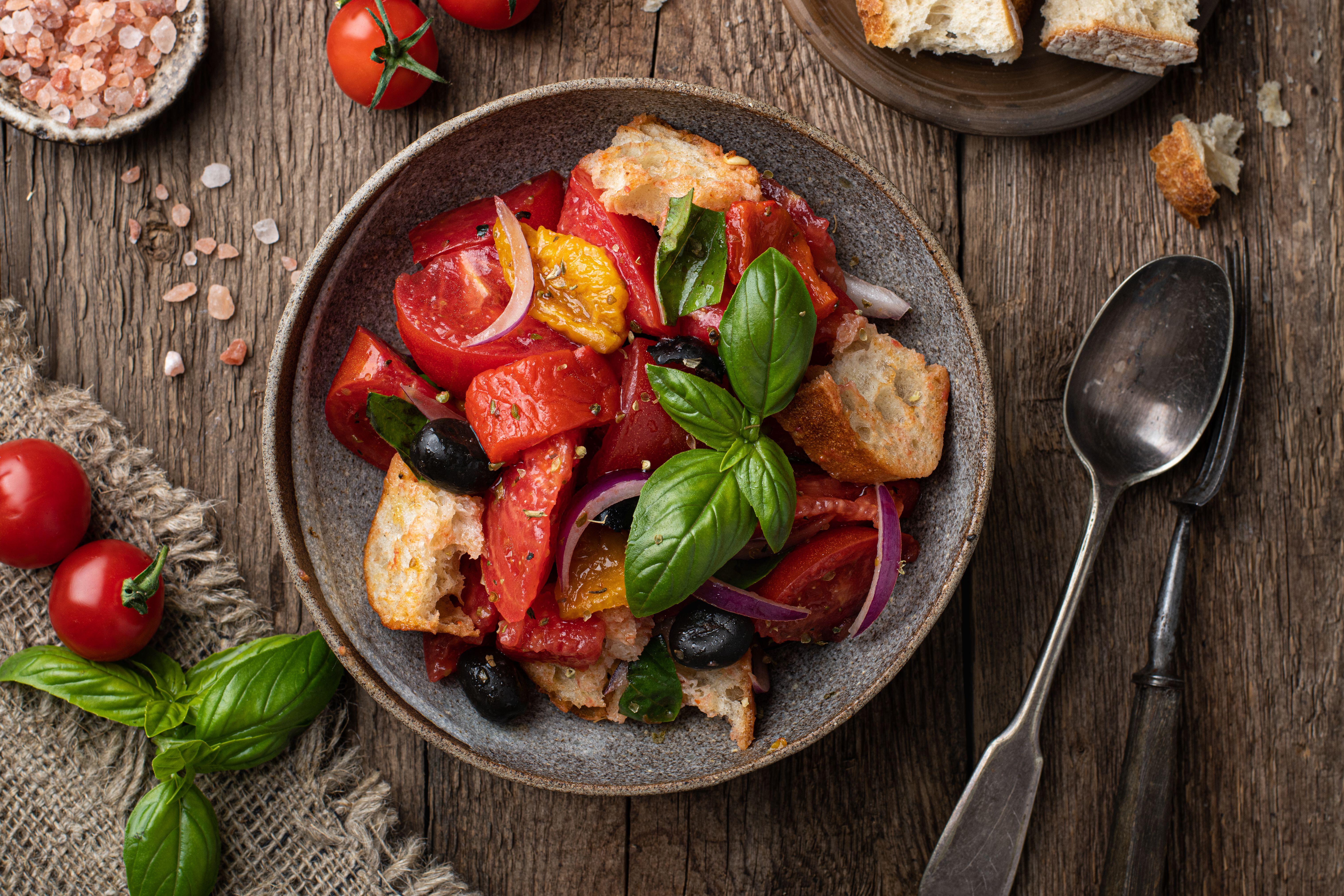 A bowl containing basil, tomatoes, bread, olives and olive oil. AKA panzanella