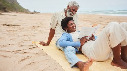 A senior couple on the beach reading.