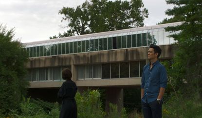 A man and woman standing outside a brutalist concrete building with large windows