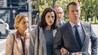 Jessica De Gouw in a grey jacket and top as Meghan and Todd Lasance in a grey suit as Jack outside court in The Secrets She Keeps.