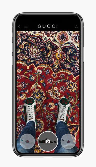 A cell phone screen with a picture of a person in jeans and tennis shoes standing on a patterned carpet.