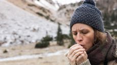 A woman blowing into her hands to warm them up