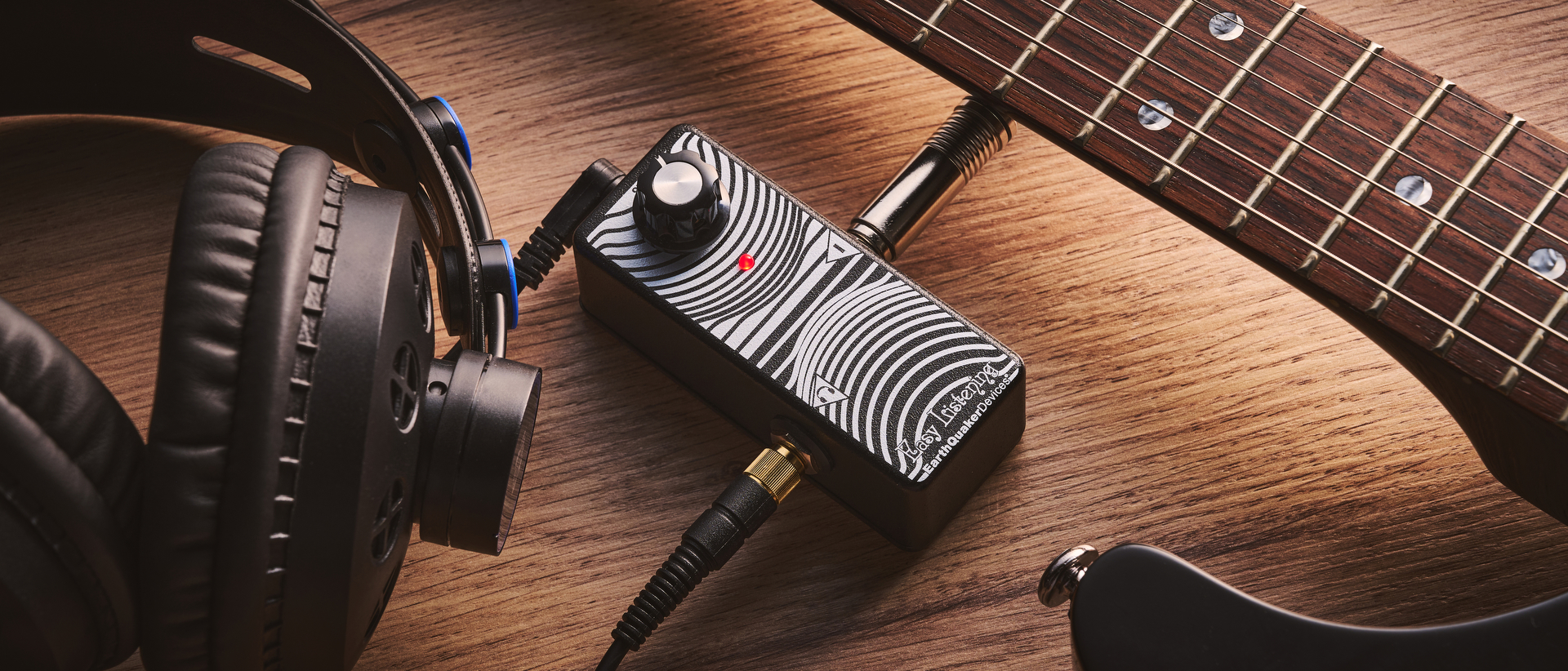 The Earthquaker Devices Easy Listening guitar headphone amp on a desk with an electric guitar and pair of headphones