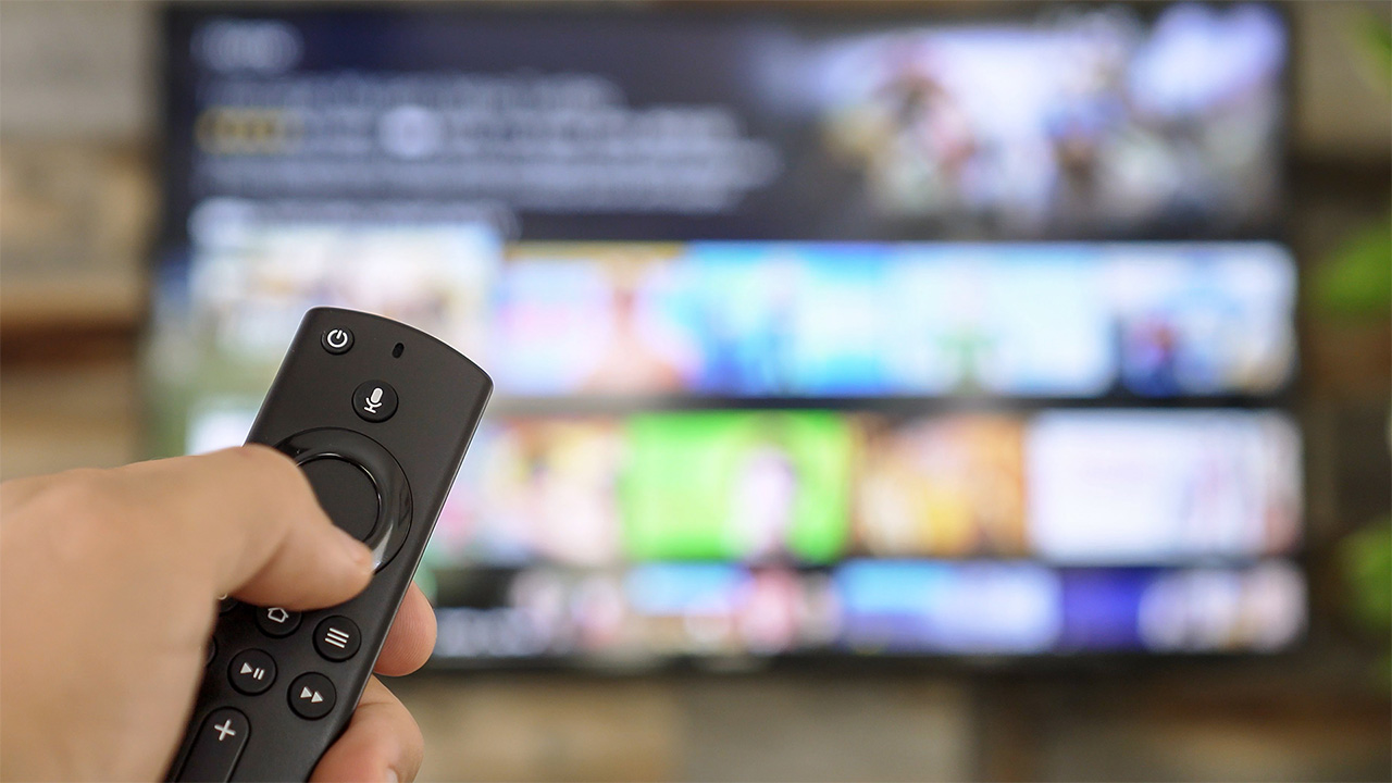 Hand holding a TV remote and using it to access a streaming service