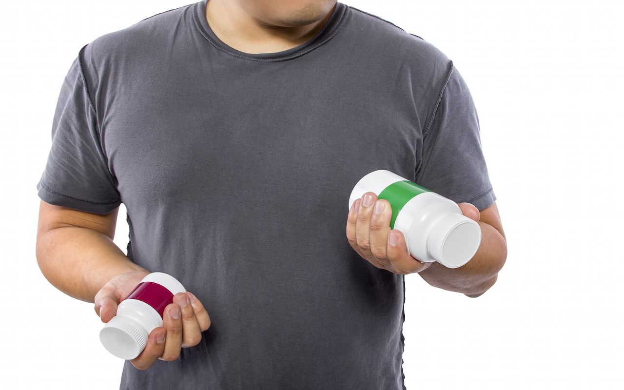 Male comparing bottles of medicine or dietary supplements.He is holding two pill bottles for comparison.The bottles have copyspace for logos.The image can also be depicting a comparison betwe