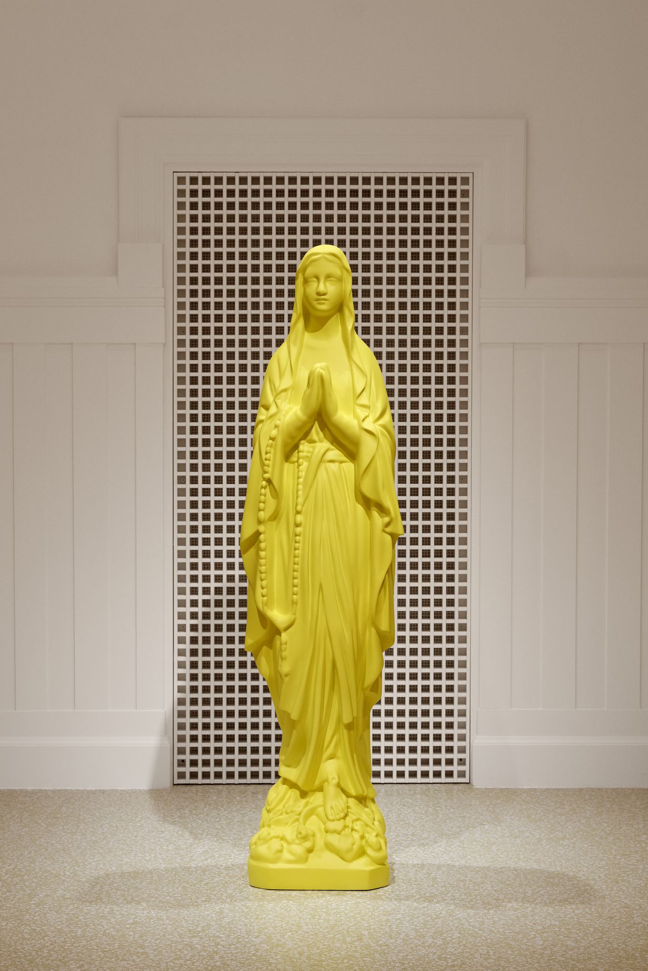 A yellow Madonna sculpture stands in a white gallery space.