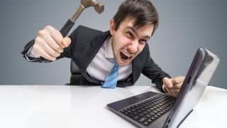 Angry and crazy man is working with laptop. He is going to damage notebook with hammer.