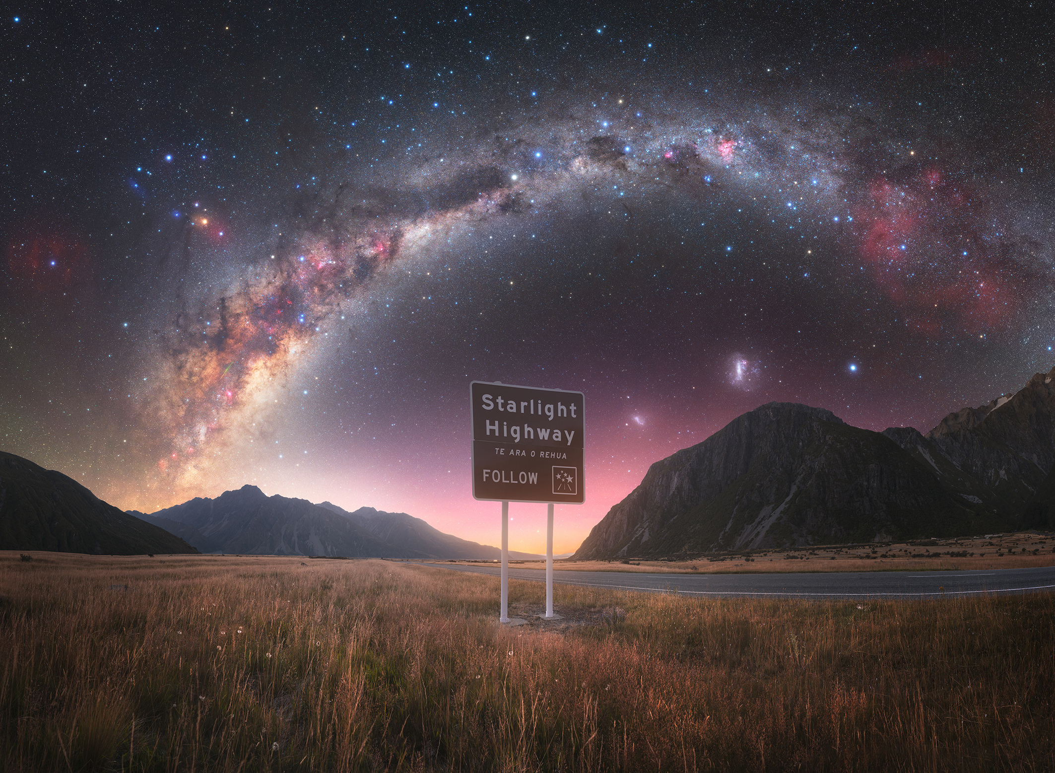 A sign for &quot;Starlight Highway&quot; against a breathtaking backdrop of the Milky Way and mountains at twilight