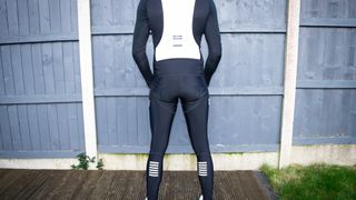 Rapha Pro Team winter bibtights from behind in front of a charming grey fence